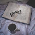cup of coffee near open book with eyeglasses
