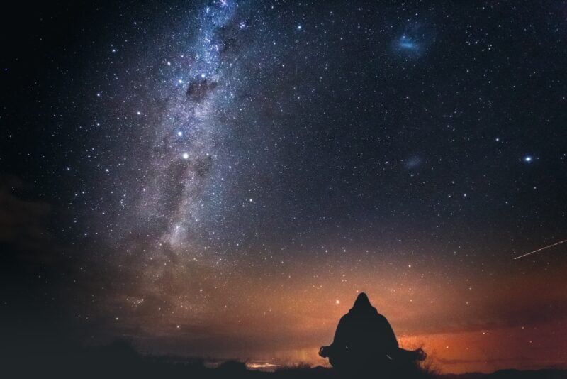 silhouette of person sitting on rock under starry night