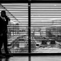 silhouette of man standing beside clear glass wall while using smartphone