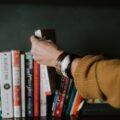 person picking white and red book on bookshelf
