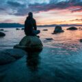 man sitting on rock surrounded by water