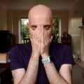 a bald man covering his face with his hands