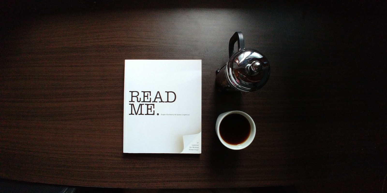 flat-lay photo of Read Me. book beside cup and silver mug on table