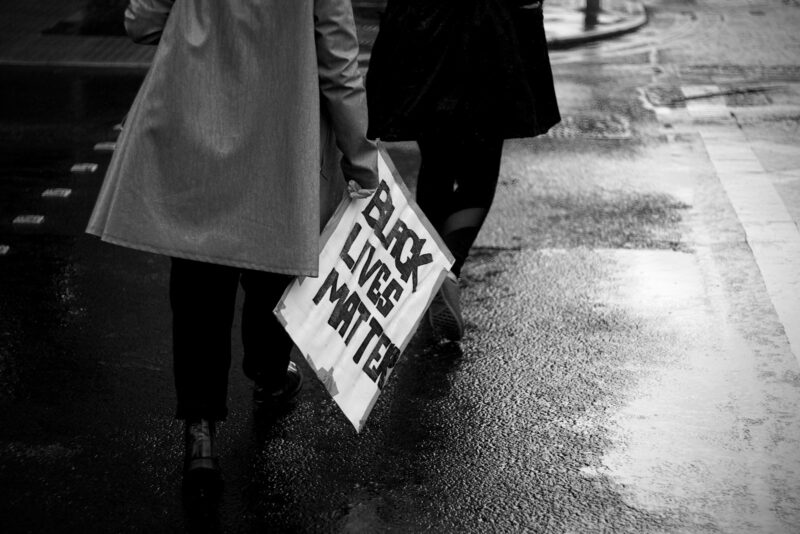 grayscale photo of person holding white and blue no smoking sign