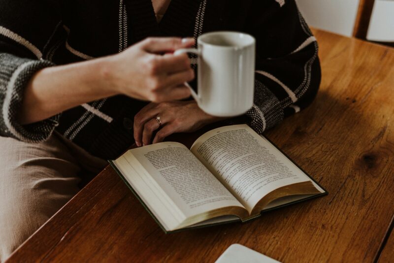 A person sitting at a table with a book and a cup of coffee
