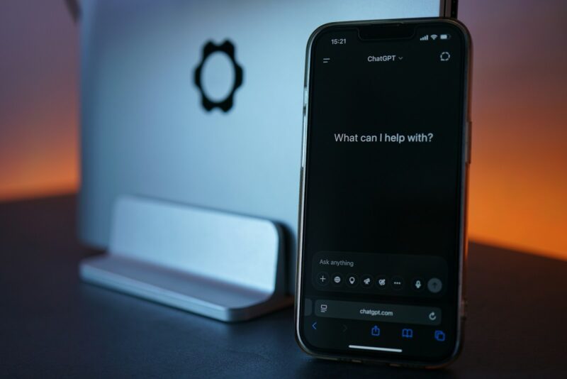 Phone displays chatgpt, next to laptop.